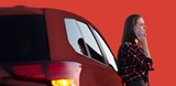 woman stands next to red car - with red background